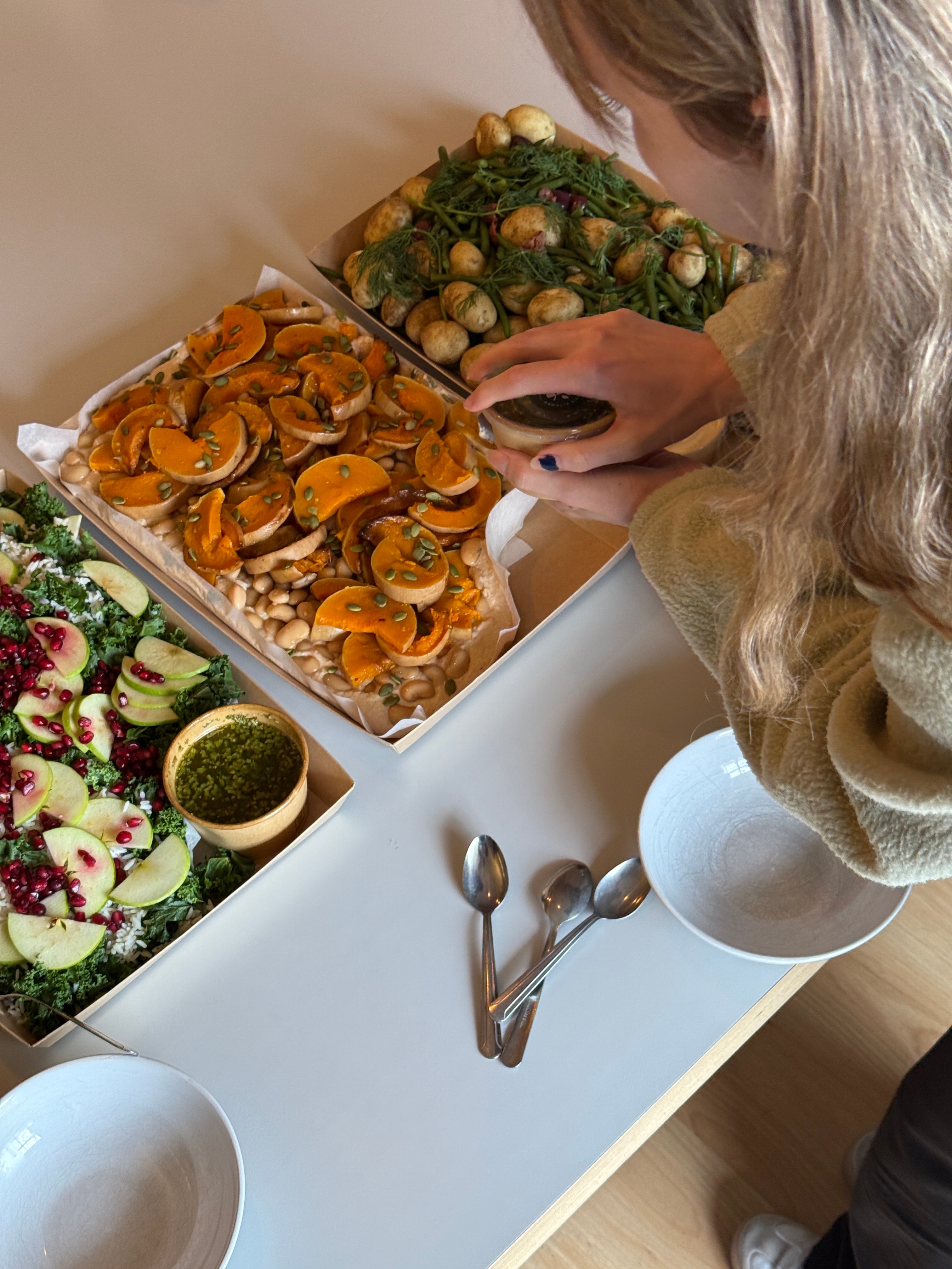 Person preparing a salad with various ingredients on a white table.