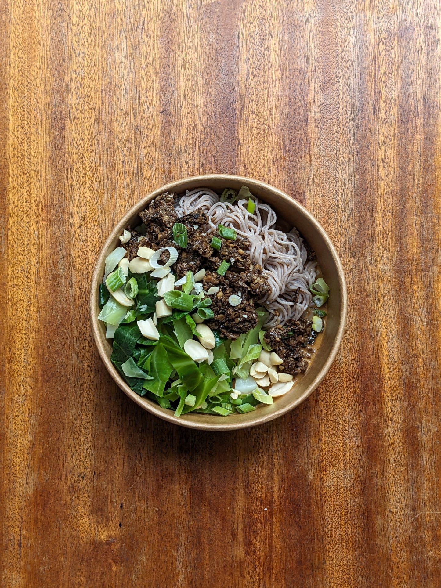 Bowl of noodles with vegetables on a wooden surface