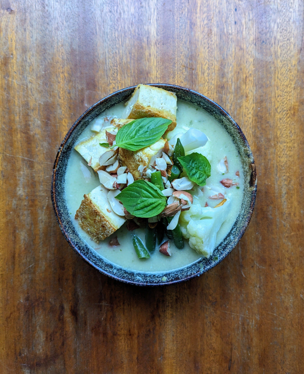Bowl of Thai curry with tofu and Thai basil on a wooden surface