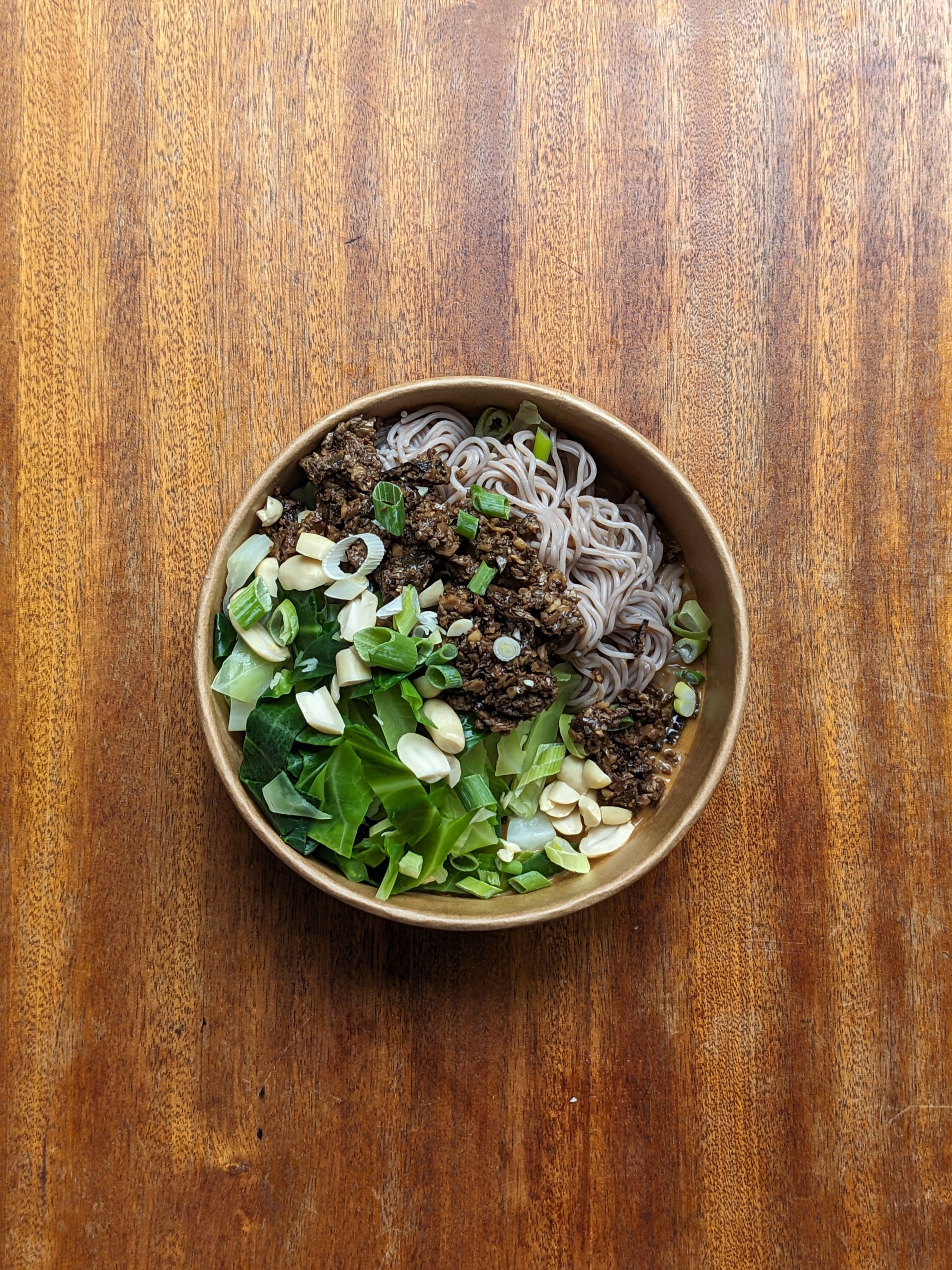 Bowl of noodles with vegetables on a wooden surface
