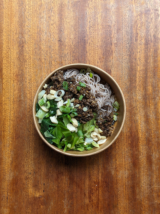 Bowl of noodles with vegetables on a wooden surface