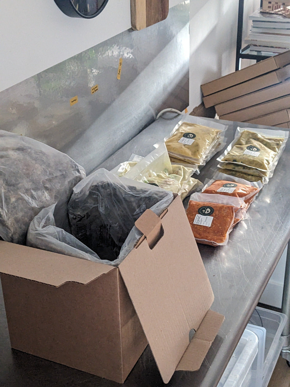 Packages of food on a metal counter next to an open cardboard box.