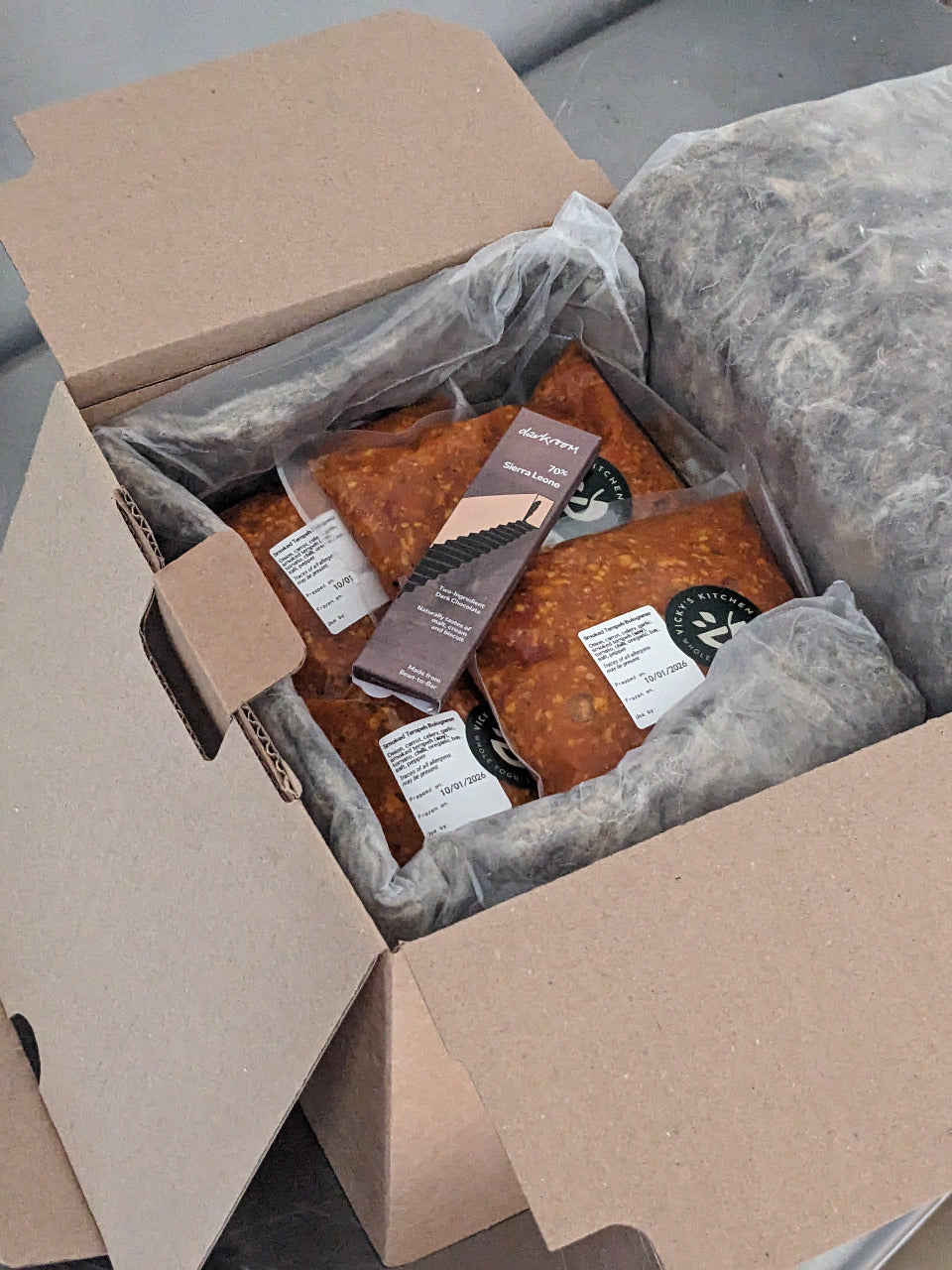 Box of packaged food items with labels on a gray surface