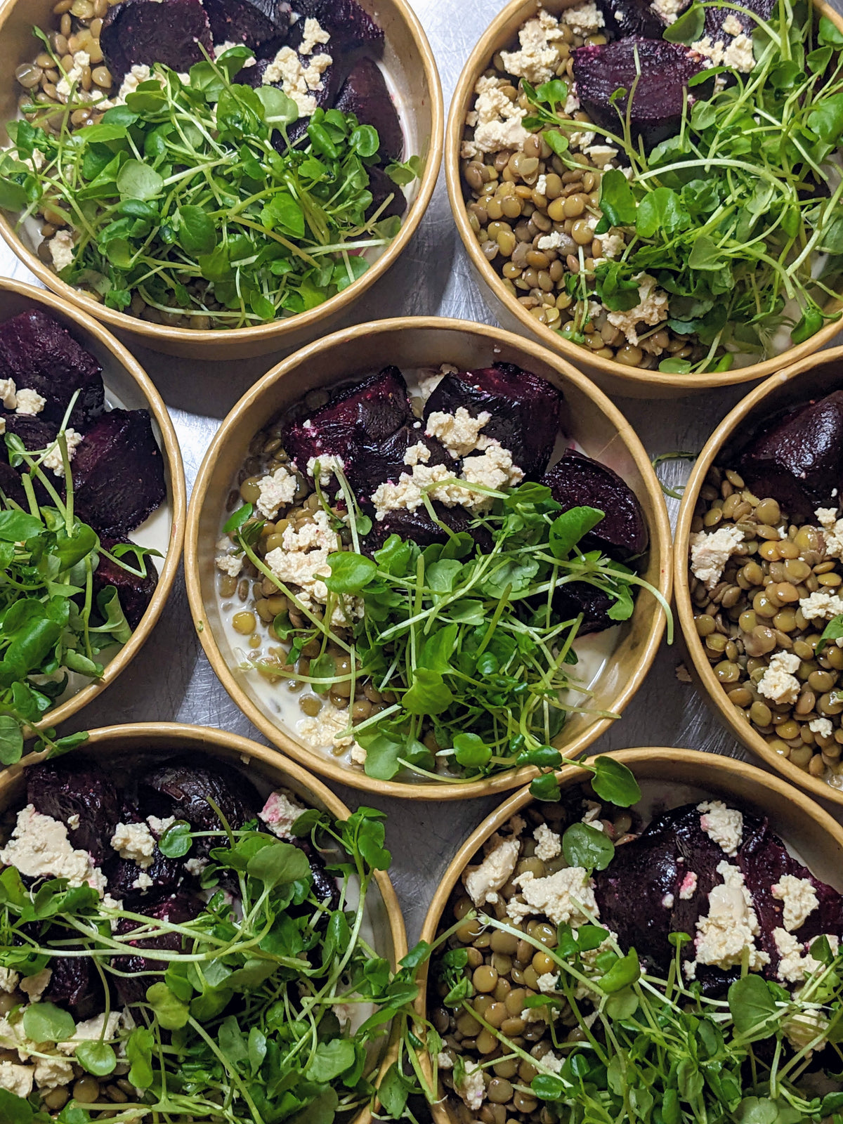 Bowls of salad with greens, beetroot, and crumbled cheese on a metal tray.